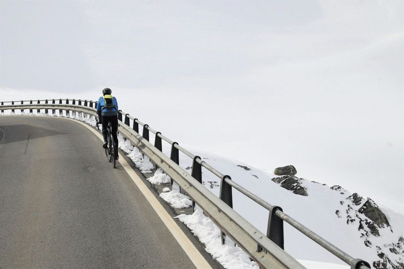 a cyclist cycling uphill next a snow mound