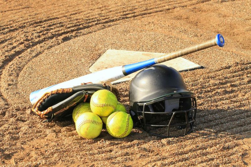 a softball bat on top of softballs and a softball helmet