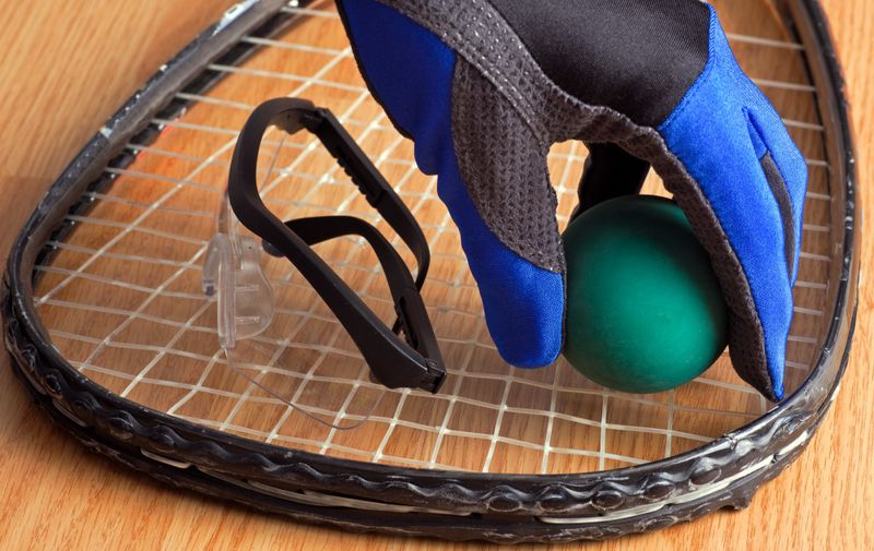 a gloved hand placing a racquetball ball on a racquet