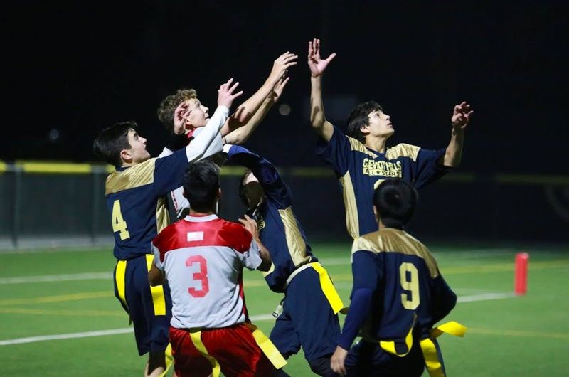 male flag football players jumping to catch a football pass