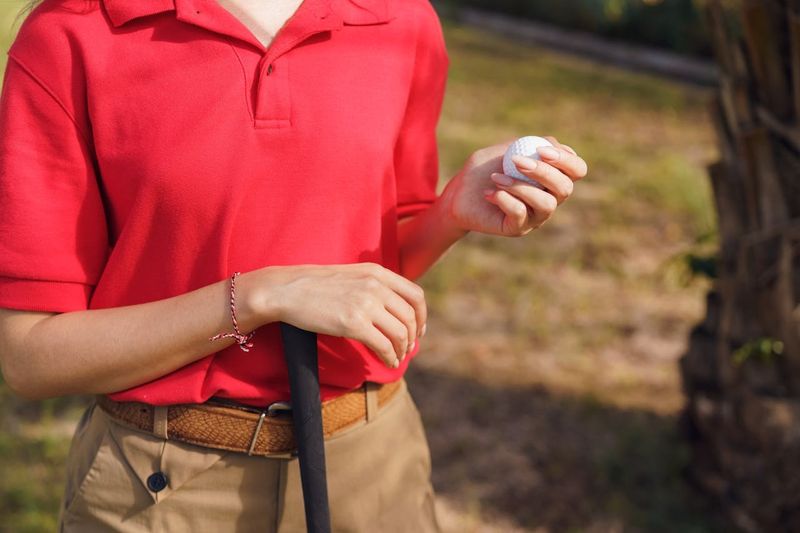 an adult female wearing a bright red golf shirt holding a golf ball and golf club