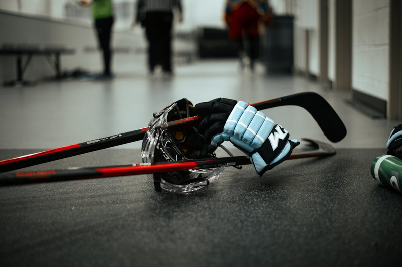 a hickey gloves lying on two hockey sticks on a locker room floor
