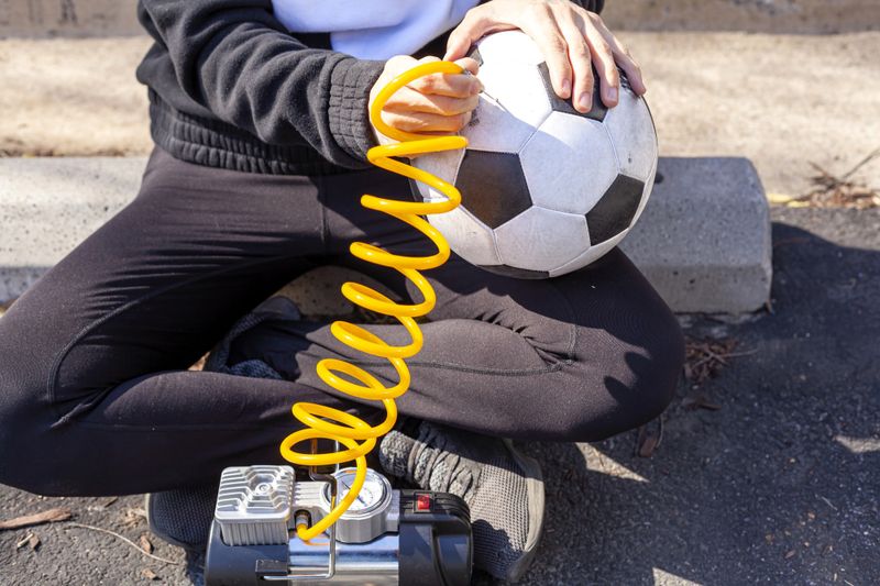 an adult female inflating a soccer ball using an air pump