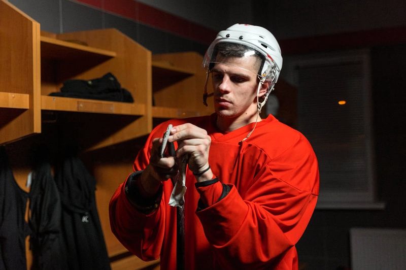 a male adult hockey player taping the blade of a hockey stick with hockey tape