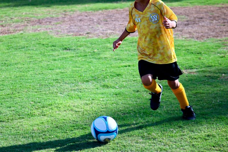 a young boy wearing football apparel about to kick a soccer ball