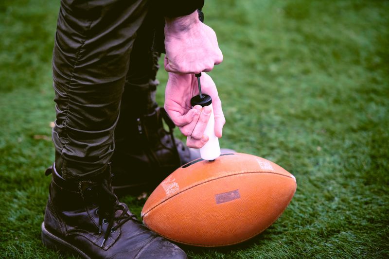 a man inflating an American football using a ball pump on grass