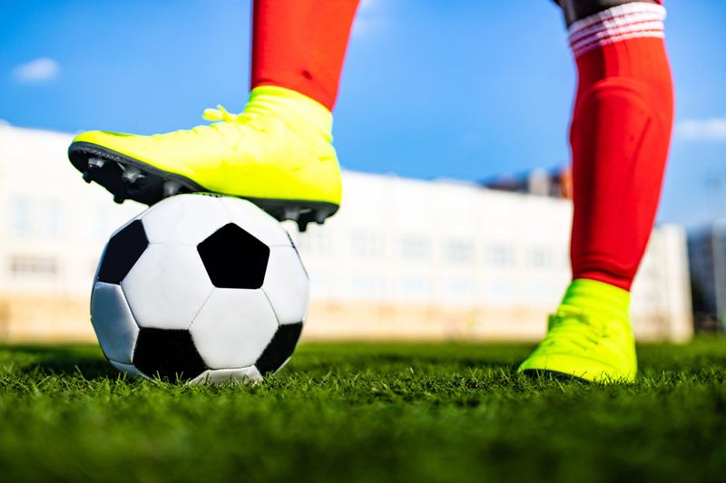 a soccer player wearing red socks with shin guards placing his foot on a soccer ball