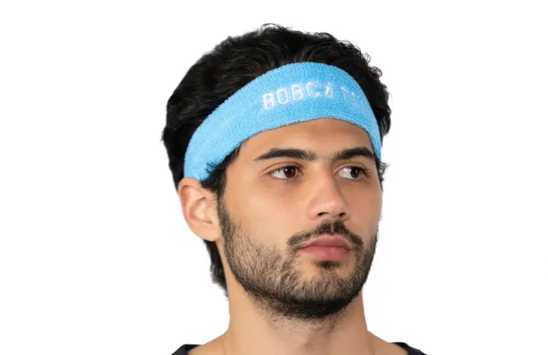 an adult male wearing a light blue headband that has the embroidered text showing the word Bobcats