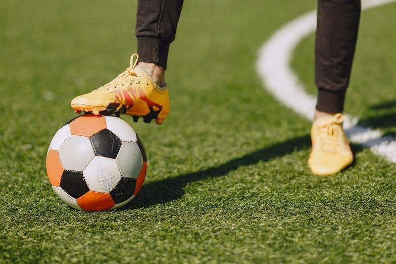 a close up of a person wearing soccer cleats with one cleat on top of a soccer ball