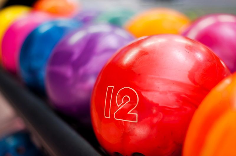 a rack of bowling balls with one red bowling ball showing the number 12