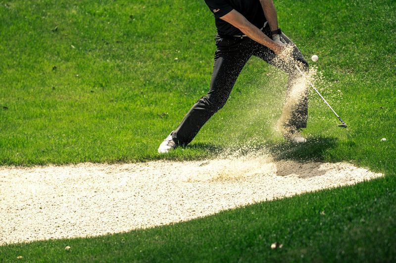 a male adult golfer hitting a club out of a sand trap