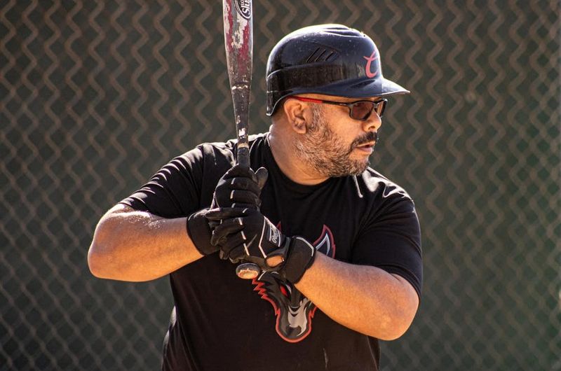 a man holding a softball bat wearing black batting gloves