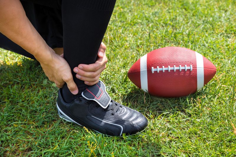 a man holding his ankle wearing football cleats next to an American football