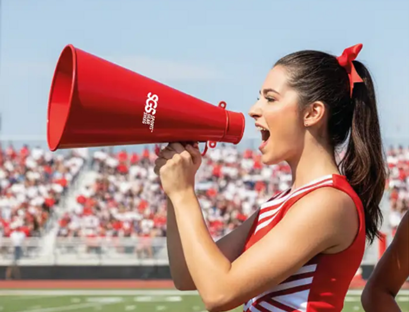 a female cheerleading shouting into a red megaphone during a football game