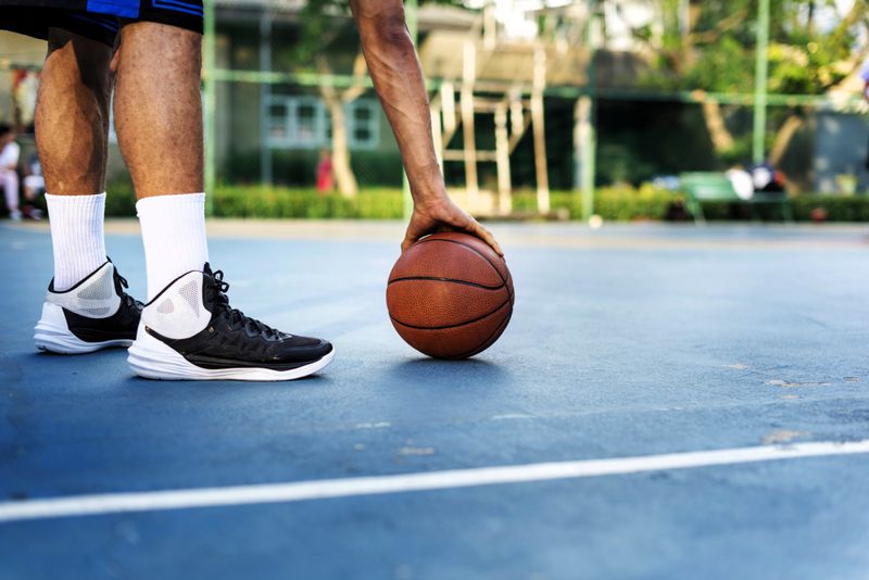 a male basketball players legs and hand holding a basketball on a blue court