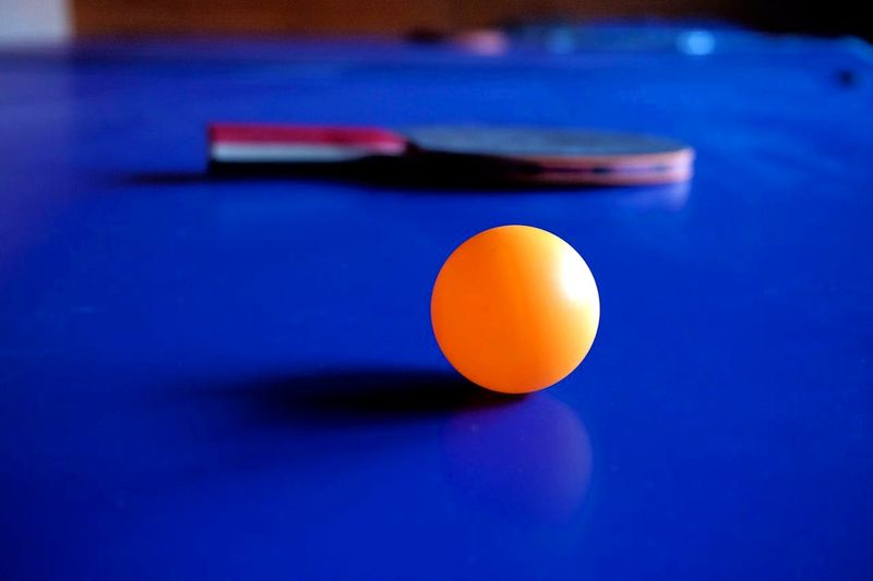 an orange ping pong ball with a ping pong paddle in the background