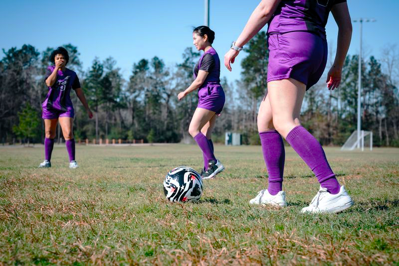 three female soccer players wearing purple soccer uniforms