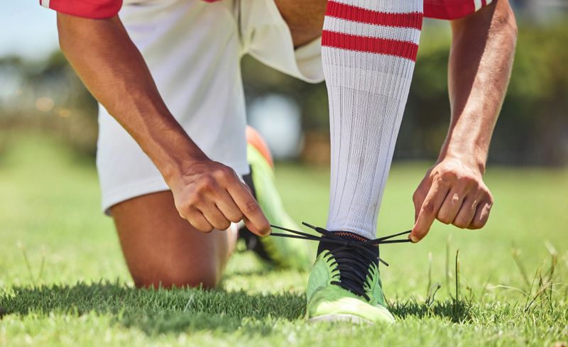 a man tying soccer cleats standing on green grass