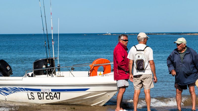 3 men standing next to a fishing boat on the shore of a beach