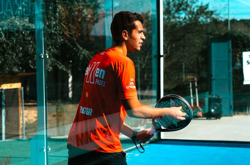 a male adult padel player holding a padel ball against his padel racket