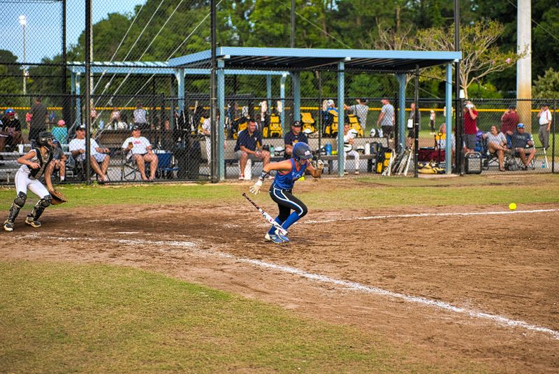 a softball tournament with spectators behind a tall fence