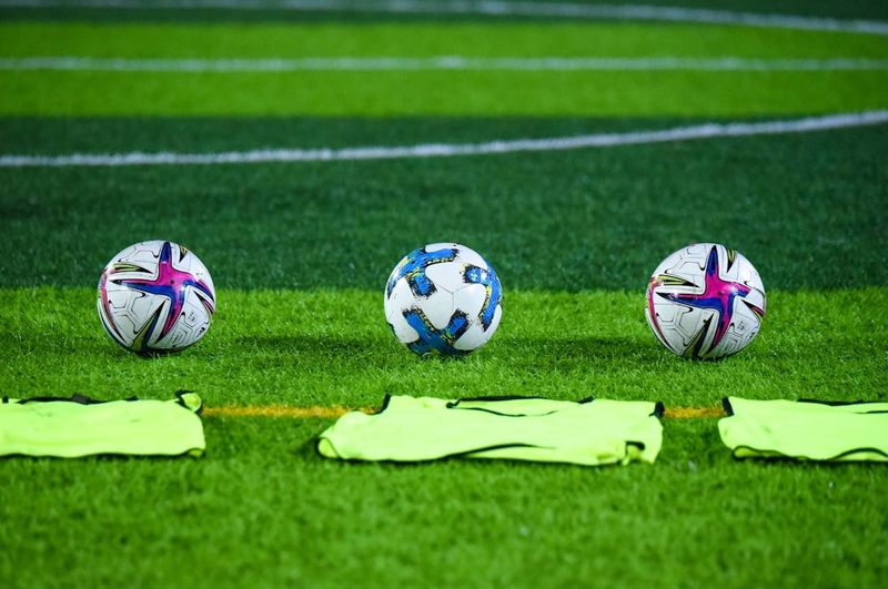 three soccer balls on grass behind green pinnies