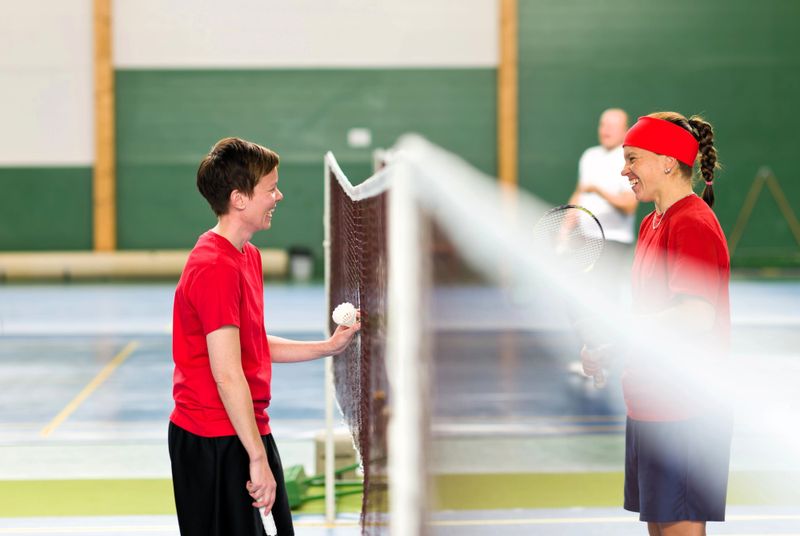two badminton players smiling at each other between the badminton net