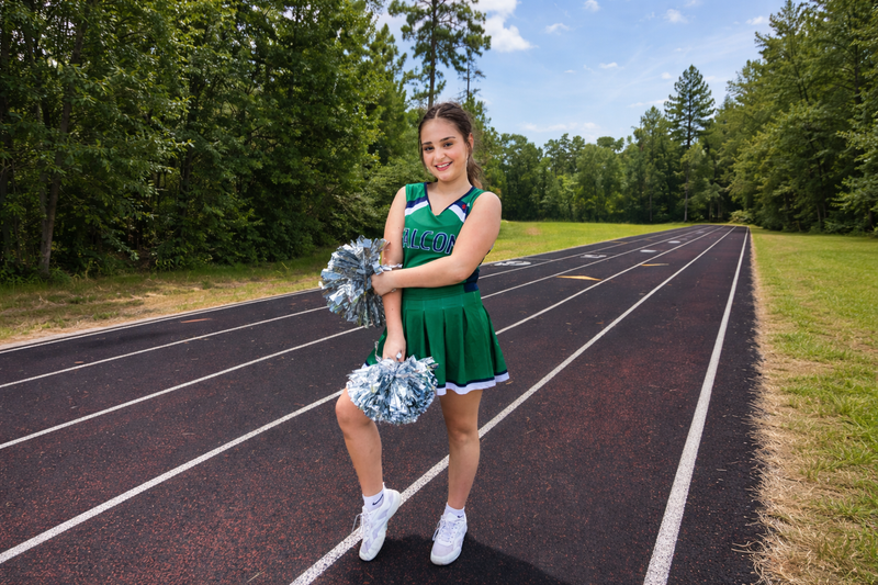 a young female cheerleader wearing a green and white cheer uniform on a running track