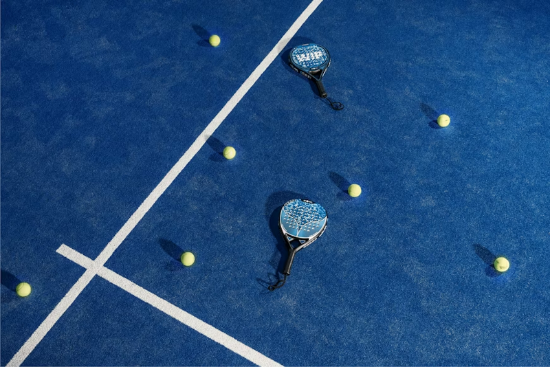 two padel rackets lying on a blue tennis court next to padel balls