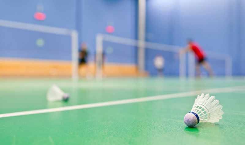 two shuttlecocks on an aqua color tennis court surface with badminton players in the backround
