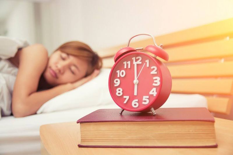 women sleeping next to an alarm clock