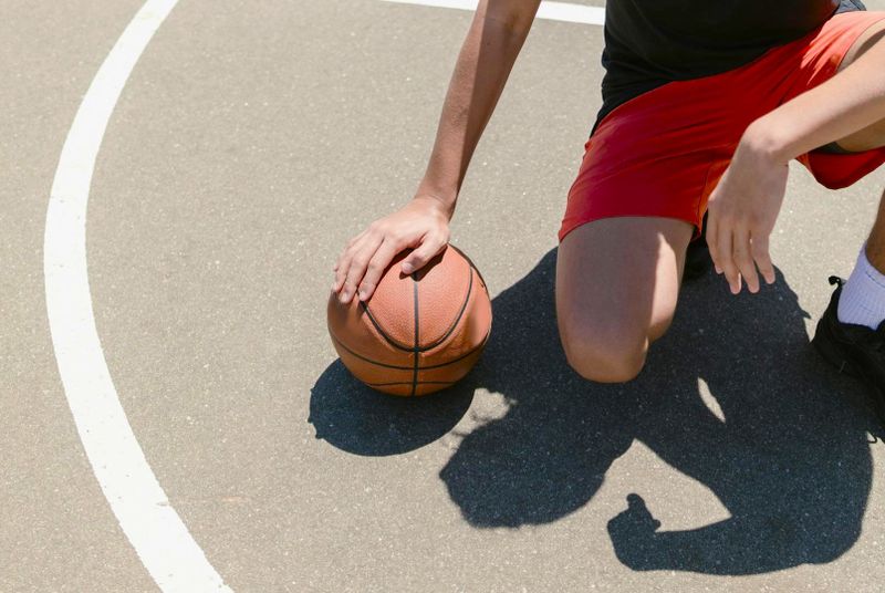 a man wearing red shorts with his hand on an outdoor basketball