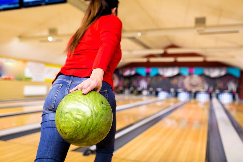 an adult female swinging a green bowling ball with her right hand