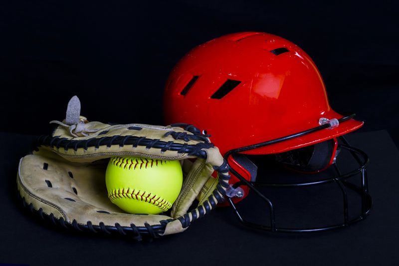 a softball inside a softball glove next to a red helment