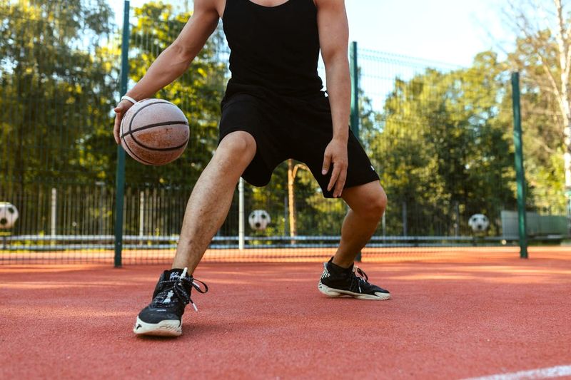 an adult male dribbling a basketball on an outdoor basketball court