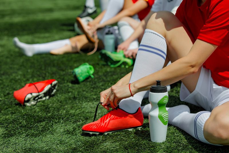 a soccer player putting on red soccer cleats while sitting on a grass