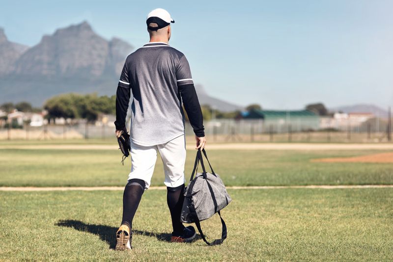 a softball player carrying a duffle bag onto a baseball field