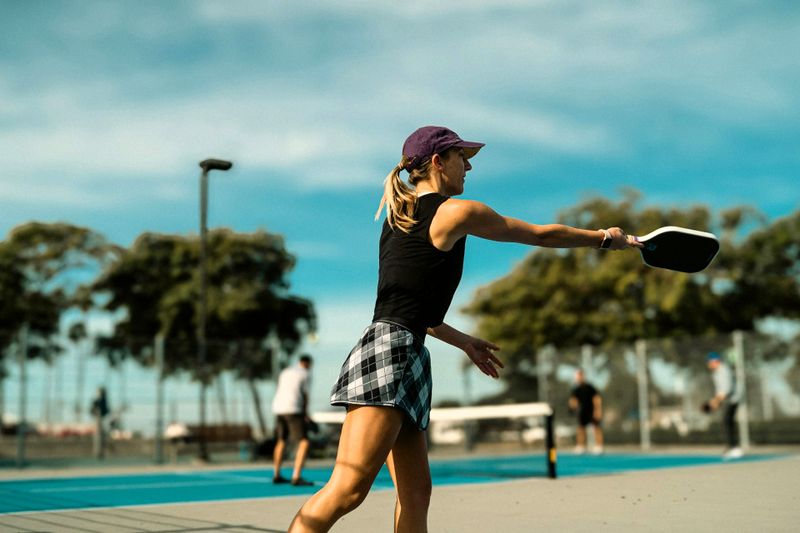 an adult female playing pickleball on an outdoor pickleball court
