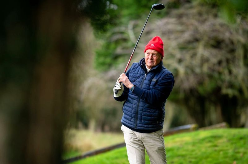 an older man playing golf in cold weather clothing