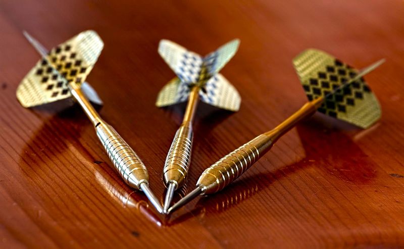 a set of three gold darts lying on a wooden table