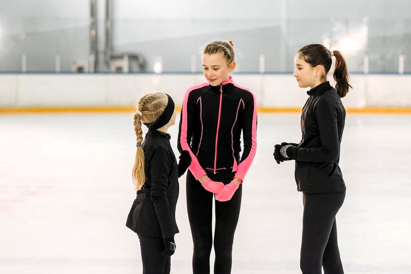 three youth figure skaters talking in a group on an ice rink