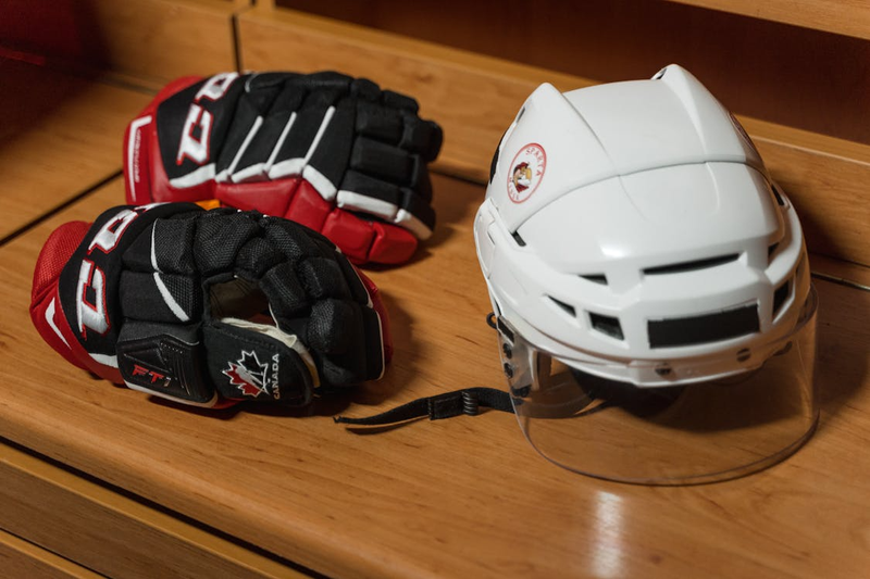 a pari of red and black hockey gloves next to a white ice hockey helmet on top of a wooden bench