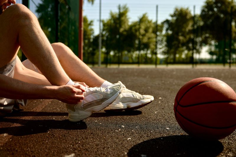 a basketball player lacing up their basketball shoes on an outdoor basketball court