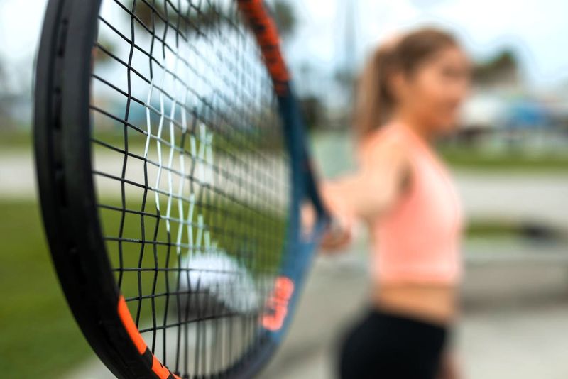 a person holding a tennis racket in focus close to the camera capturing the image