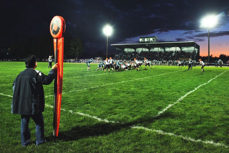 a linesman in a winter coat watching an outdoor football game