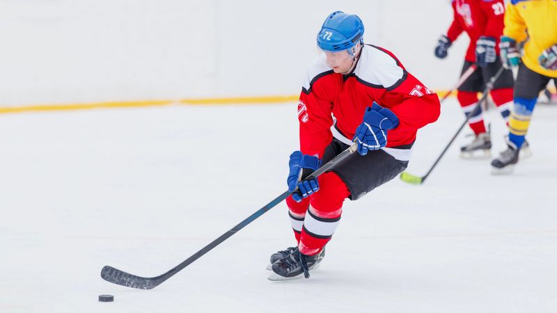 a male adult hockey player wearing a red hockey uniform skating on ice