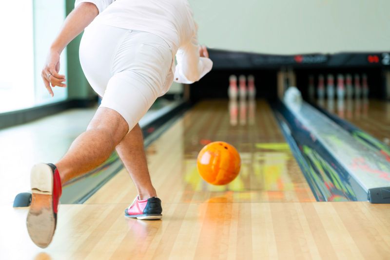 a male adult bowling an orange bowling ball