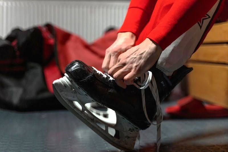 a close up image of an ice hockey skate and hands tying laces