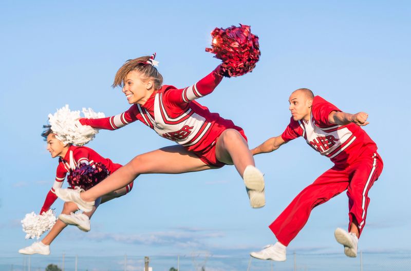 three cheerleaders in red and white uniforms posing in the air during a cheer routine